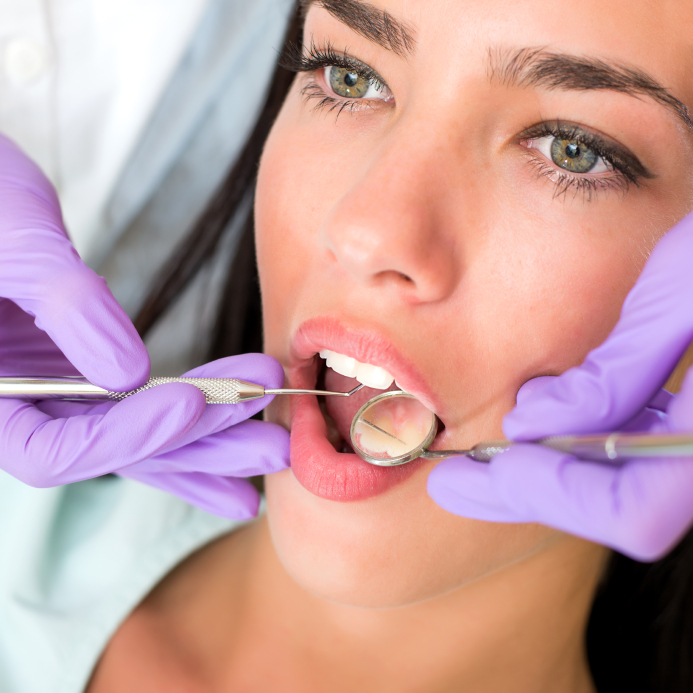 A woman in a dentist chair while the dentist checks her teeth.