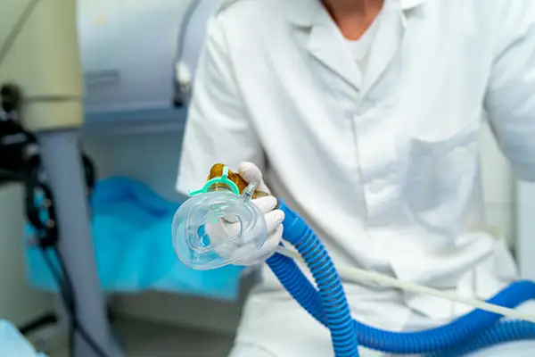 Dentist holding a sedation mask connected to a nitrous oxide system in a dental clinic.